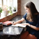 Young woman seated at table and writing in a notebook.